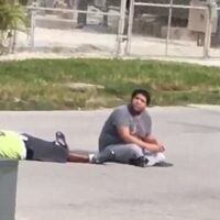 Arnaldo Rios sitting on the street with charles kinsey with his hands up