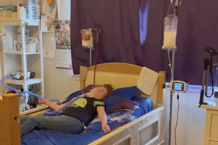 Medically fragile girl lying in a hospital bed with IV bags and medical equipment.